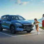BYD SEALION 5 DM-i preț România | iDevice.ro Family charges an electric SUV at a waterfront overlook, with a man plugging in the car as a child runs toward it and a woman watches nearby.