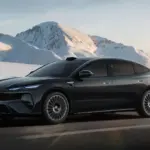 BYD Seal 08 verde | iDevice.ro Black sedan driving on a snow-covered mountain road with alpine peaks in the background.