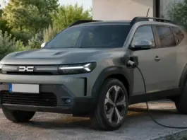 Gray SUV plugged into a wall-mounted electric vehicle charger outdoors by a house, with cable attached to the front side port and visible greenery nearby.