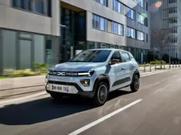 Silver compact SUV driving along a city street with modern glass-fronted buildings on both sides, motion blurred lanes.