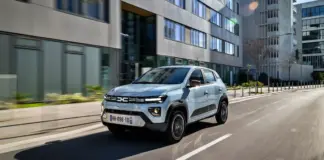 Silver compact SUV driving along a city street with modern glass-fronted buildings on both sides, motion blurred lanes.