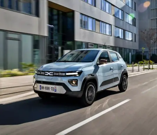 Silver compact SUV driving along a city street with modern glass-fronted buildings on both sides, motion blurred lanes.