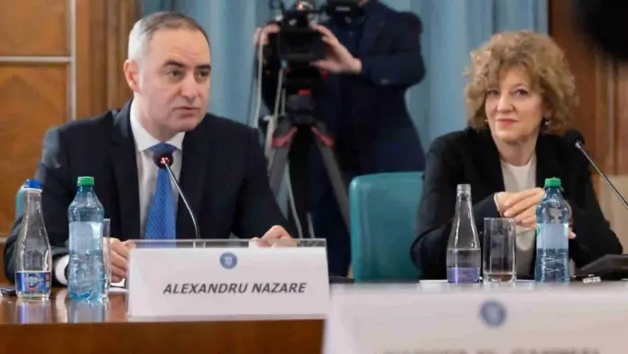 Two conference delegates seated at a panel table: a man in a dark suit and blue tie on the left and a woman with curly hair on the right, with microphones and water bottles in front; a nameplate reads 'ALEXANDRU NAZARE'.