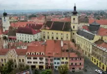 Estimarile Meteo ale Starii Vremii pentru Romania cu Evolutia in Regiunile Tarii din 16 Iulie 2026 Aerial view of a historic town with red-tiled roofs and pastel buildings, dominated by a pale yellow baroque-style complex with a tall clock tower.