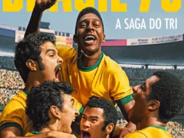 Soccer teammates in yellow jerseys celebrate a goal, lifting a player as a packed stadium cheers behind them.