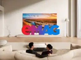 Modern living room with curved white sofas, a landscape painting, and oversized colorful 'EMAG' letters in front; two people lie on yoga mats on the floor in the foreground.