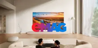 Modern living room with curved white sofas, a landscape painting, and oversized colorful 'EMAG' letters in front; two people lie on yoga mats on the floor in the foreground.