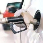 Prețurile Benzinei și Motorinei Nu vor Reveni la Valorile Dinaintea Războiului din Iran foarte Curând | iDevice.ro Close-up of a fueling nozzle inserted into a car's fuel filler at a gas station, beige and black nozzle with hose visible