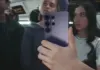 Resigilate eMAG, Samsung GALAXY S26, S25, Z Flip si Z Fold la Preturi REDUSE cu 1.999 LEI Person on a bus takes a selfie with a purple smartphone, other passengers blur in the background.