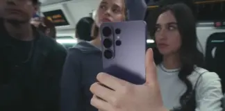 Person on a bus takes a selfie with a purple smartphone, other passengers blur in the background.