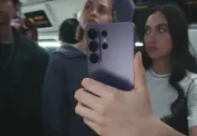 Samsung GALAXY S26 cu 2.269 LEI Pret REDUS la eMAG, S26 Plus si S26 Ultra Ieftine Person on a bus or train holds a purple smartphone up to take a selfie, with other passengers in the background.
