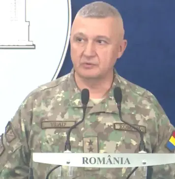Situația CRITICĂ la Granița României, AVERTISMENTUL de ULTIMĂ ORĂ al Șefului Armatei Military officer in camouflage speaking at a podium during a briefing, with a blue backdrop and 'ROMÂNIA' visible on the sign.