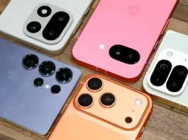 Several iPhone models with prominent camera bumps arranged on a wooden surface, showing white, pink, blue, orange, and green backs and multiple lenses per phone.
