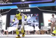 Robotii Inlocuiesc Oamenii in Totalitate, Imaginile SPECTACULOASE Publicate in China (VIDEO) Yellow humanoid robot performs on a stage in Shanghai, China, with spectators and other robots nearby. (Informative caption: 'Shanghai, China' visible on stage)