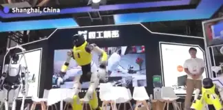 Yellow humanoid robot performs on a stage in Shanghai, China, with spectators and other robots nearby. (Informative caption: 'Shanghai, China' visible on stage)