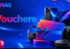 Blue promotional banner with gadgets (laptop, headphones) and a gift box with blue ribbon, suggesting vouchers and prizes from eMAG.