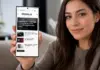 Woman holding a smartphone showing the iDevice.ro news site on the screen while smiling at the camera