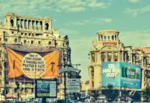 AVERTIZARI Cod ROSU si PORTOCALIU Meteo de ULTIM MOMENT Emise de ANM pentru Romania pe 3 August 2026 Historic city street with ornate old buildings, blue sky, and large orange banner in the foreground displaying Romanian text.