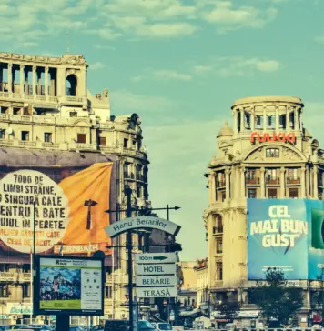 AVERTIZARI Cod ROSU si PORTOCALIU Meteo de ULTIM MOMENT Emise de ANM pentru Romania pe 3 August 2026 Historic city street with ornate old buildings, blue sky, and large orange banner in the foreground displaying Romanian text.
