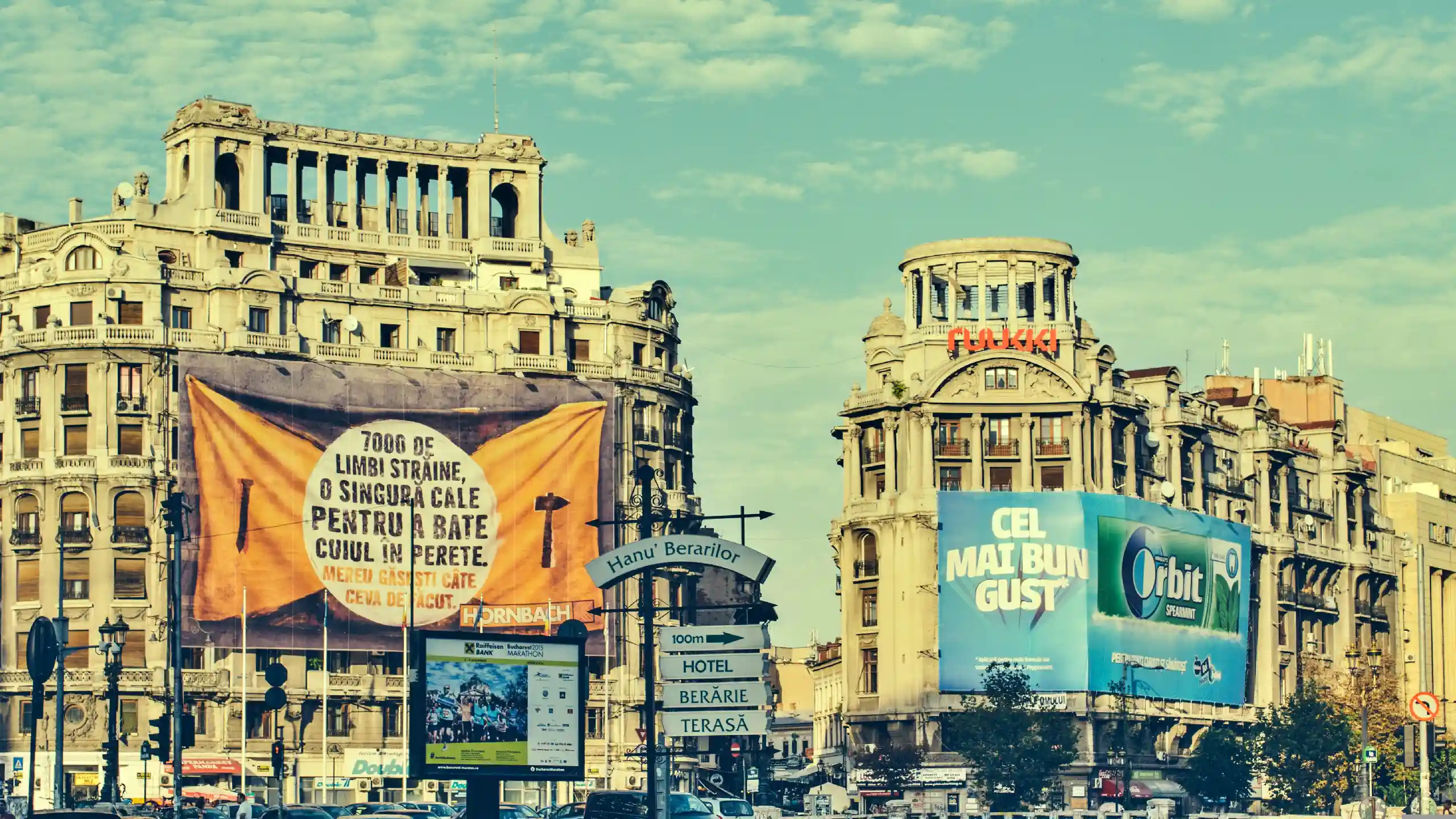 Historic city square with ornate, classical buildings and large orange banner in the foreground.