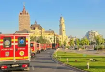 Avertizarile Meteo Cod ROSU si PORTOCALIU Emise de ANM cu Vreme Extrema in Romania pe 4 August 2026 Line of red emergency ambulances (Pompierii/SMURD) driving along a city street past historic yellow stone buildings under a clear blue sky, with green grass and trees on the right.