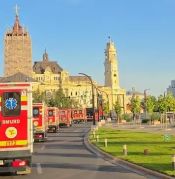 Avertizarile Meteo Cod ROSU si PORTOCALIU Emise de ANM cu Vreme Extrema in Romania pe 4 August 2026 Line of red emergency ambulances (Pompierii/SMURD) driving along a city street past historic yellow stone buildings under a clear blue sky, with green grass and trees on the right.
