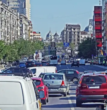 Benzina si Motorina Inca Scumpe dupa Legea pentru Criza Petroliera Busy city avenue filled with cars, taxis, and a bus in heavy traffic between green trees on the left and tall buildings with billboards on the right.