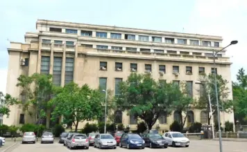 Cadastrul: Vestea Proasta de la ANCPI pentru Cand se Redeschide eTerra Facade of a large beige office building with rows of windows, green trees, and a parking lot in the foreground.