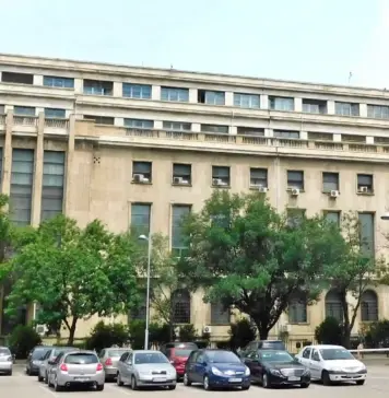Cadastrul: Vestea Proasta de la ANCPI pentru Cand se Redeschide eTerra Facade of a large beige office building with rows of windows, green trees, and a parking lot in the foreground.