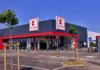 Exterior of a Kaufland supermarket with grey facade, red trim, and two large Kaufland signs against a blue sky