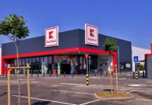 Exterior of a Kaufland supermarket with grey facade, red trim, and two large Kaufland signs against a blue sky