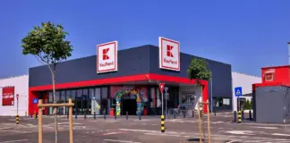 Exterior of a Kaufland supermarket with grey facade, red trim, and two large Kaufland signs against a blue sky