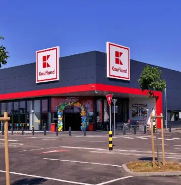Catalogul Kaufland cu Ofertele Speciale din Magazine pentru 2 August 2026 Exterior of a Kaufland supermarket with grey facade, red trim, and two large Kaufland signs against a blue sky