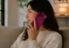 Data Lansarii iPhone 18 Pro, Cand Incep Precomenzile si Livrarile Woman sitting on a sofa, talking on a pink smartphone held to her ear, in a cozy living room with warm lighting.