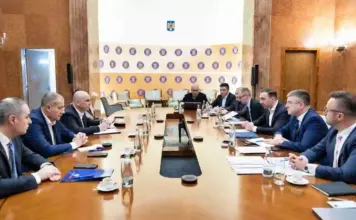 Guvernul Interimar Bolojan a Avertizat Oficial Comisia Europeana Formal boardroom meeting with executives seated along a long wooden table; microphones, documents and water glasses on the table.