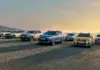 Row of modern SUVs lined up on a gravel surface at sunset, with mountains in the distance on the left.
