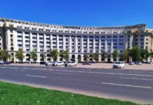 Masura ANCPI pentru Cand se Redeschide Cadastrul si Accesul la Aplicatia eTerra Curved white multi-story building with many windows and arches along a busy street, cars parked in front on a sunny day.