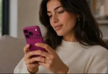 Woman sitting on a sofa, looking at a pink smartphone in her hands indoors