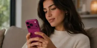 Woman sitting on a sofa, looking at a pink smartphone in her hands indoors