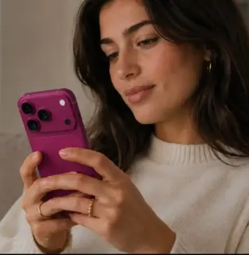 Sper ca iPhone 18 Pro sa Nu Fie Atat de Scump Precum Spune Acest Analist Woman sitting on a sofa, looking at a pink smartphone in her hands indoors