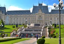 Starea de Alerta va Lasa in Bezna Unele Orase din Romania, Explicatiile Primarului din Iasi Grand historic palace with symmetrical towers, central staircase, and manicured gardens under a blue sky; visitors on the lawn.