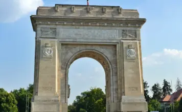 Stone triumphal arch with carved panels and medallions, set against a clear blue sky.