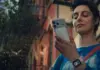 Young woman outdoors, checking her smartphone, wearing a blue shirt and a crossbody bag.