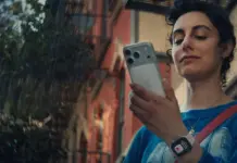 Young woman outdoors, checking her smartphone, wearing a blue shirt and a crossbody bag.