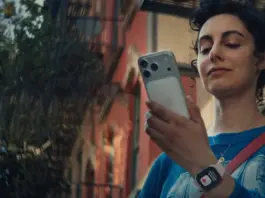 Young woman outdoors, checking her smartphone, wearing a blue shirt and a crossbody bag.