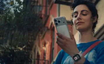 iOS 27 Confirma Aceste 6 Noi Modele de Telefoane iPhone Young woman outdoors, checking her smartphone, wearing a blue shirt and a crossbody bag.