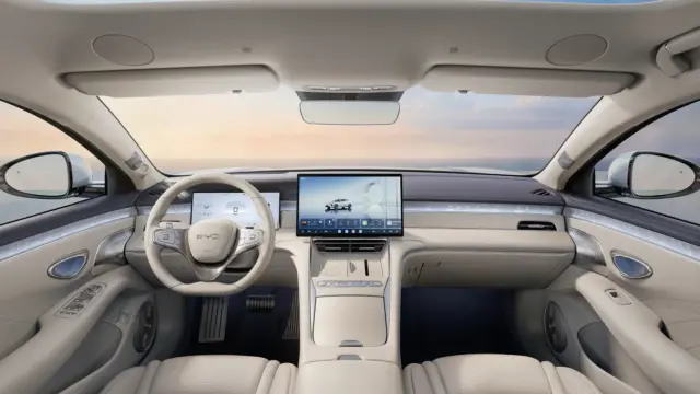 Luxurious car interior with cream leather seats, a wide central touchscreen, and a digital instrument cluster amid a panoramic view outside the windshield