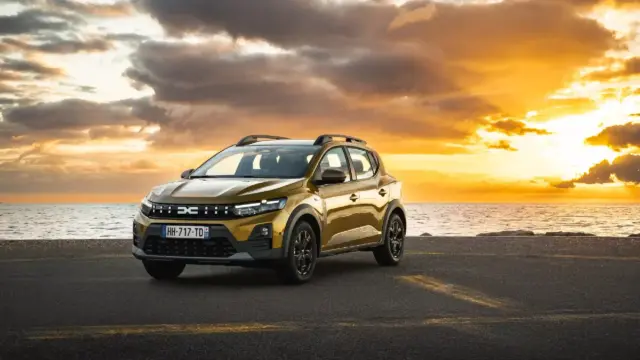 Golden SUV parked on a coastal road at sunset with the sea and orange sky in the background.