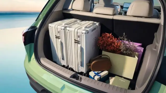 Open car trunk filled for a trip: two silver hard-shell suitcases, a bouquet of flowers, and gift boxes toward the back of a green SUV.