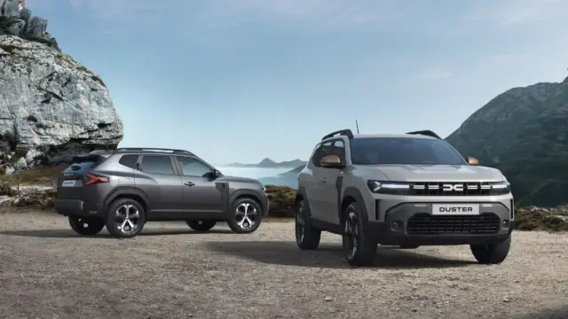 Two silver Dacia Duster SUVs parked on a rocky mountain pass with cliffs and distant peaks in the background.